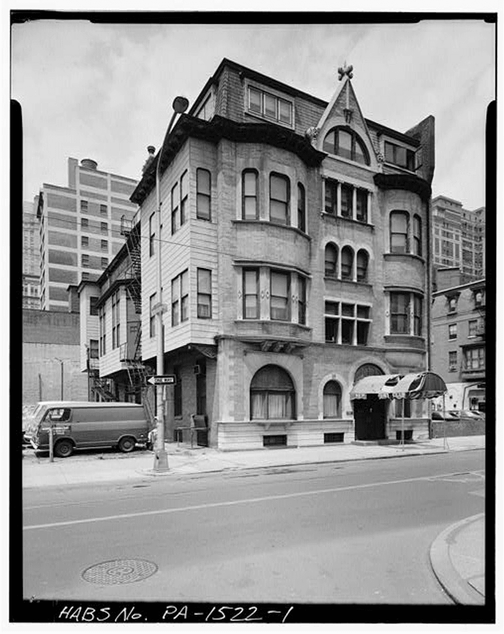 Black & white photo of a gracious five-story city building with a stone front, arches and bay windows.