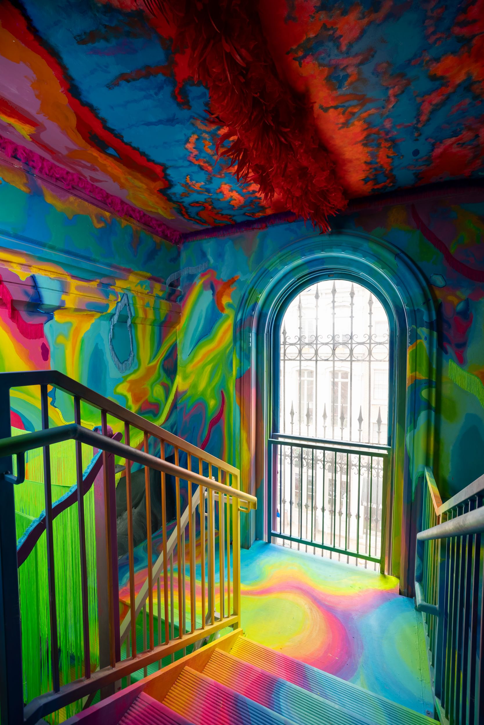 View from the top level of a 19th-century stairwell with a large arched window, walls covered with a psychedelic mural.