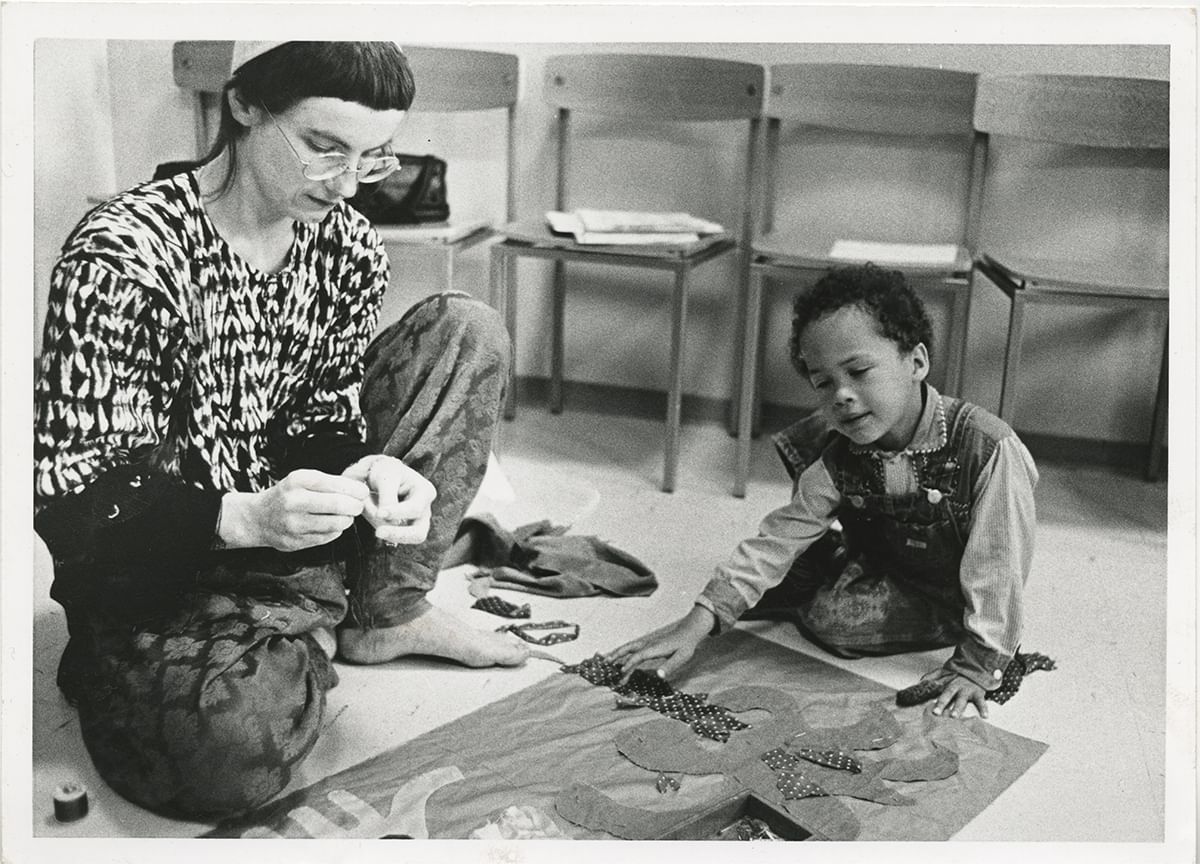 Vintage black & white photo of Cherry and her young child sitting comfortably on the floor, working on a piece of fabric art.