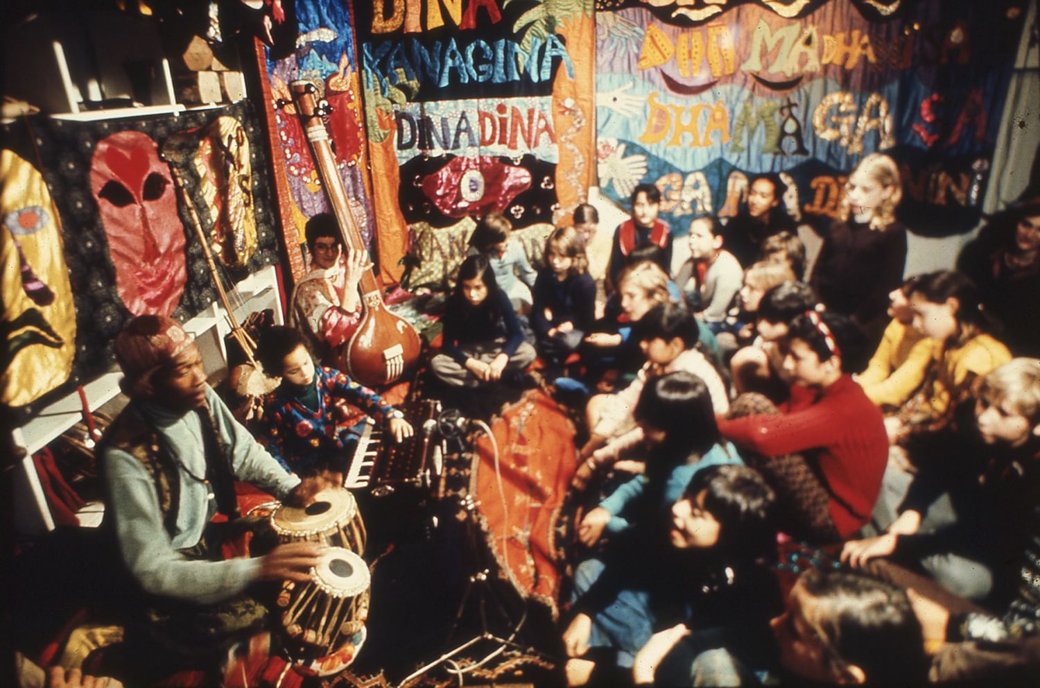 At left, the Cherry family plays instruments for dozens of kids sitting on the ground, surrounded by large-scale textile art