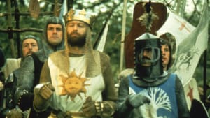 Outdoors. Men dressed in knights armor, one has a sun with a mustache on the front, the other has a tree design