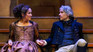 In sumptuous period costumes, Peakes and Hernandez sit side by side sharing a longing look, lightly touching hands