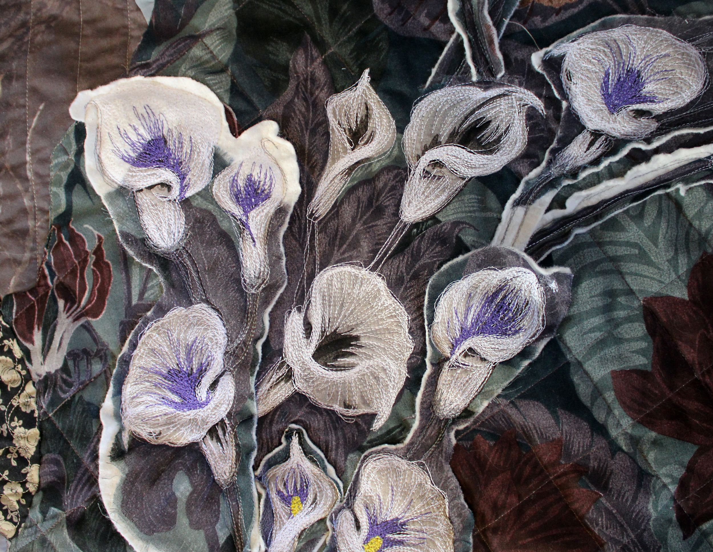 Close-up on dynamic white and purple embroidered lilies on a dark quilted fabric background.