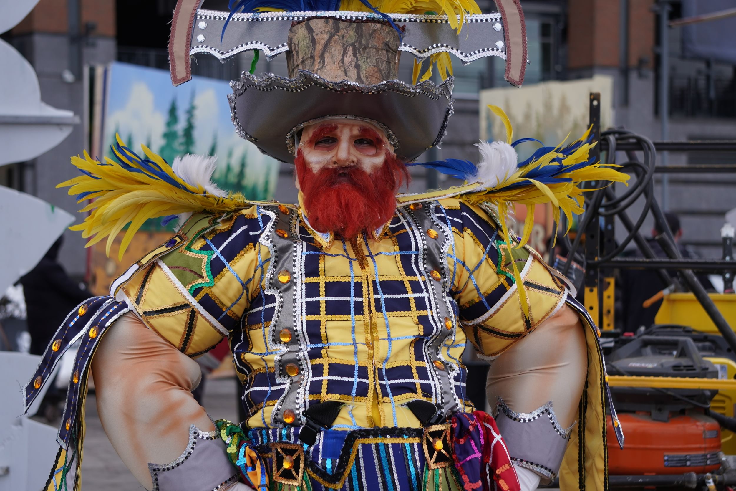 Gregario poses with hands on hips in a lumberjack costume with huge arms, a bushy red beard, sequins & giant feather epaulets