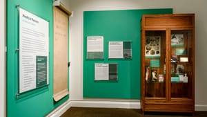 Exhibit view: signage about medical racism on green walls, with a tall wooden cabinet of medical specimens at right.