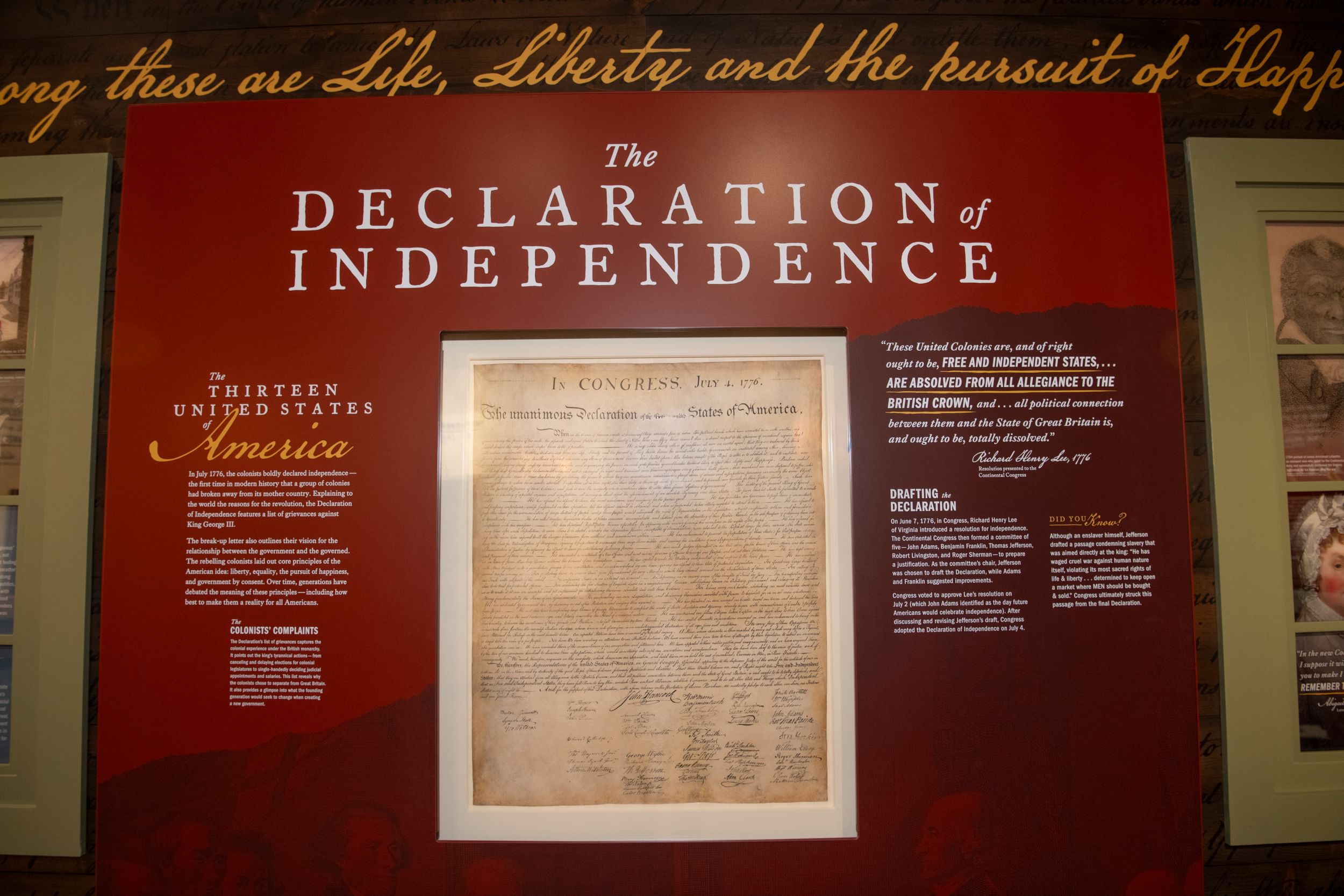 Large glass display in a maroon wall with white text shows the 1823 Stone engraving of the Declaration, brown with age.