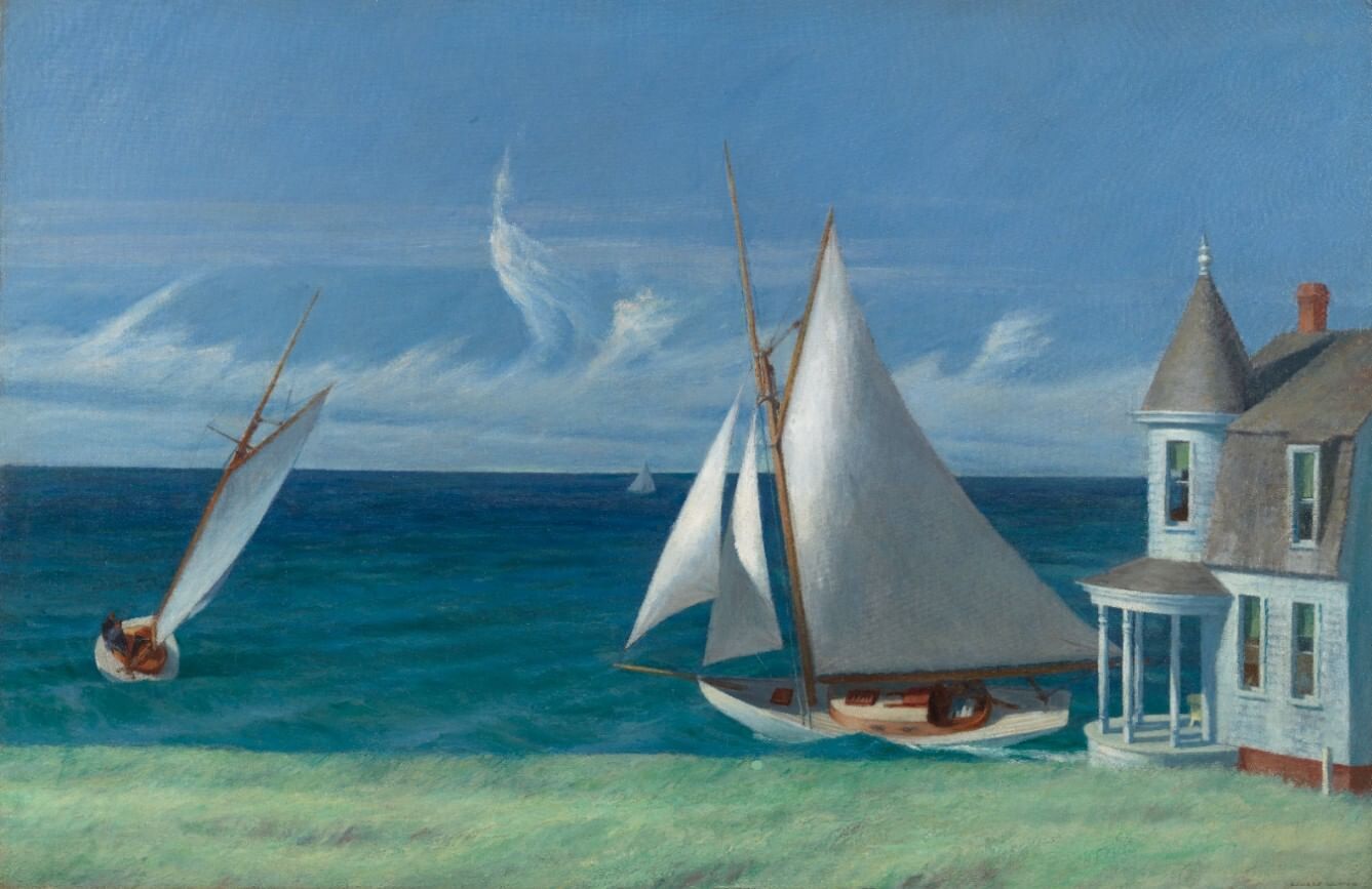 Sunny view of two sailboats on a turquoise sea seen over a grassy shore, with a Victorian-style house in the right corner