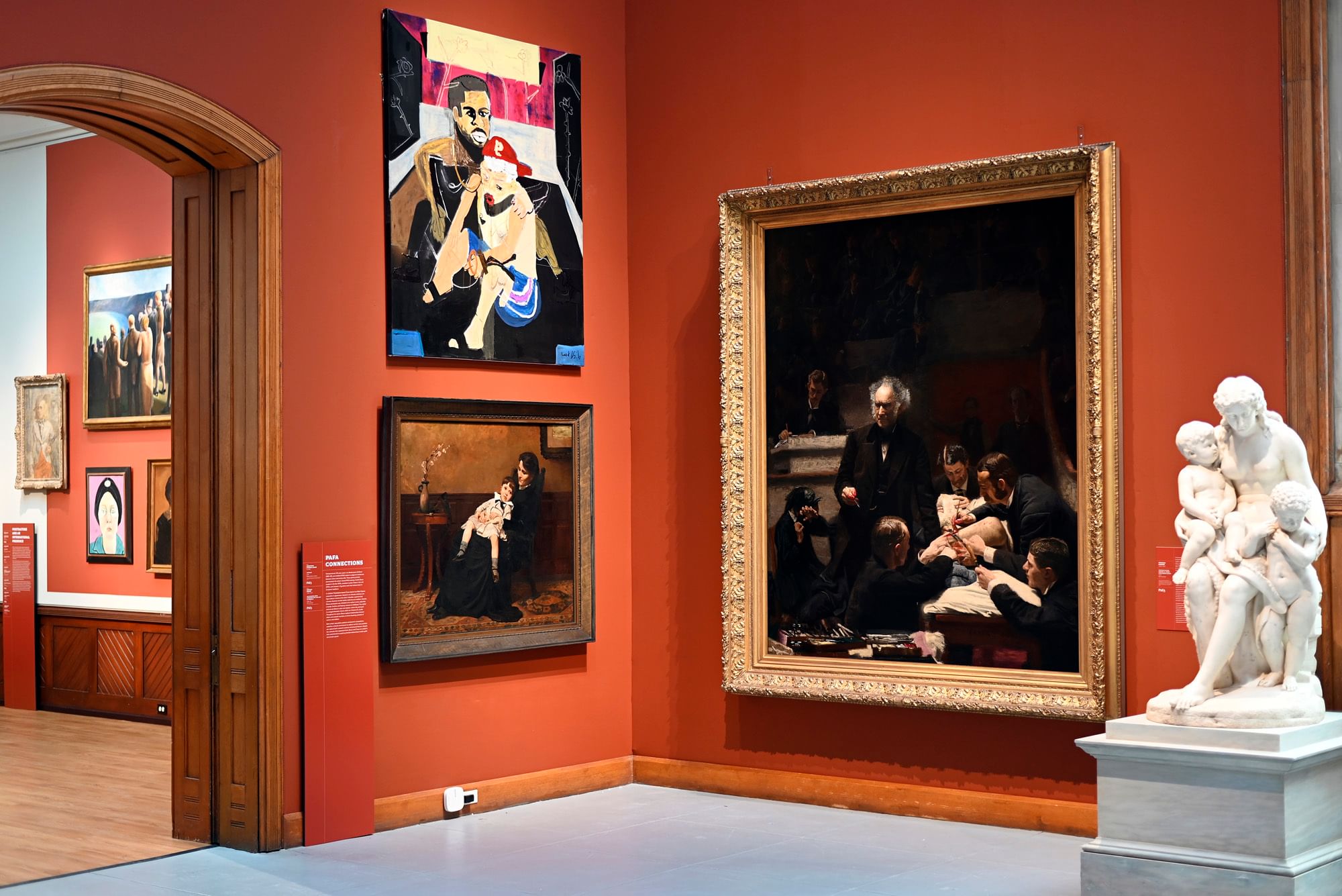 Rust-colored gallery view with a marble statue of a woman & children, Eakins’ The Gross Clinic & a modern abstract painting