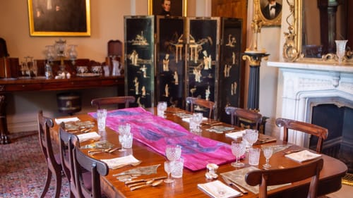 Fine wooden dining table in a 19th century room, set with crystal glassware, silver utensils, and glass art instead of plates