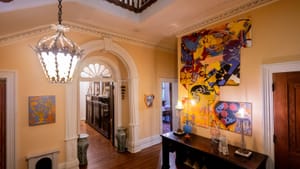 A lantern-like chandelier lights the mansion’s entry space, which has arched doorways and fancy molding setting off the art.