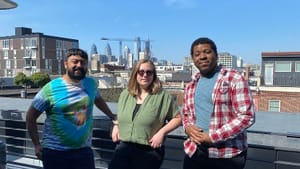 Neil, Alaina & Kyle lean on the railing of a 4th-floor roof-deck on a sunny day, the Philly skyline behind them