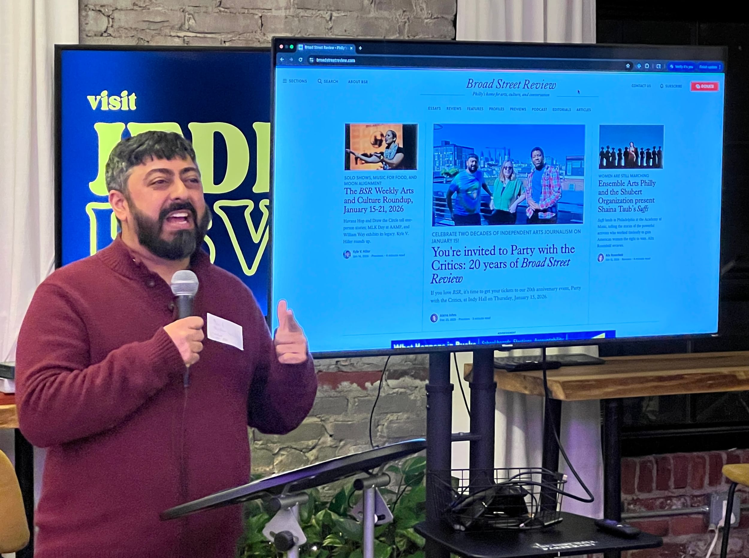 Closeup on Neil, a bearded Indian American man wearing a maroon sweater, smiling and speaking into a mic.