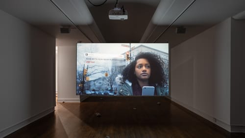 Gallery view of video screen showing a pop-up notification on a man with a gun, next to a young Black woman’s impassive face