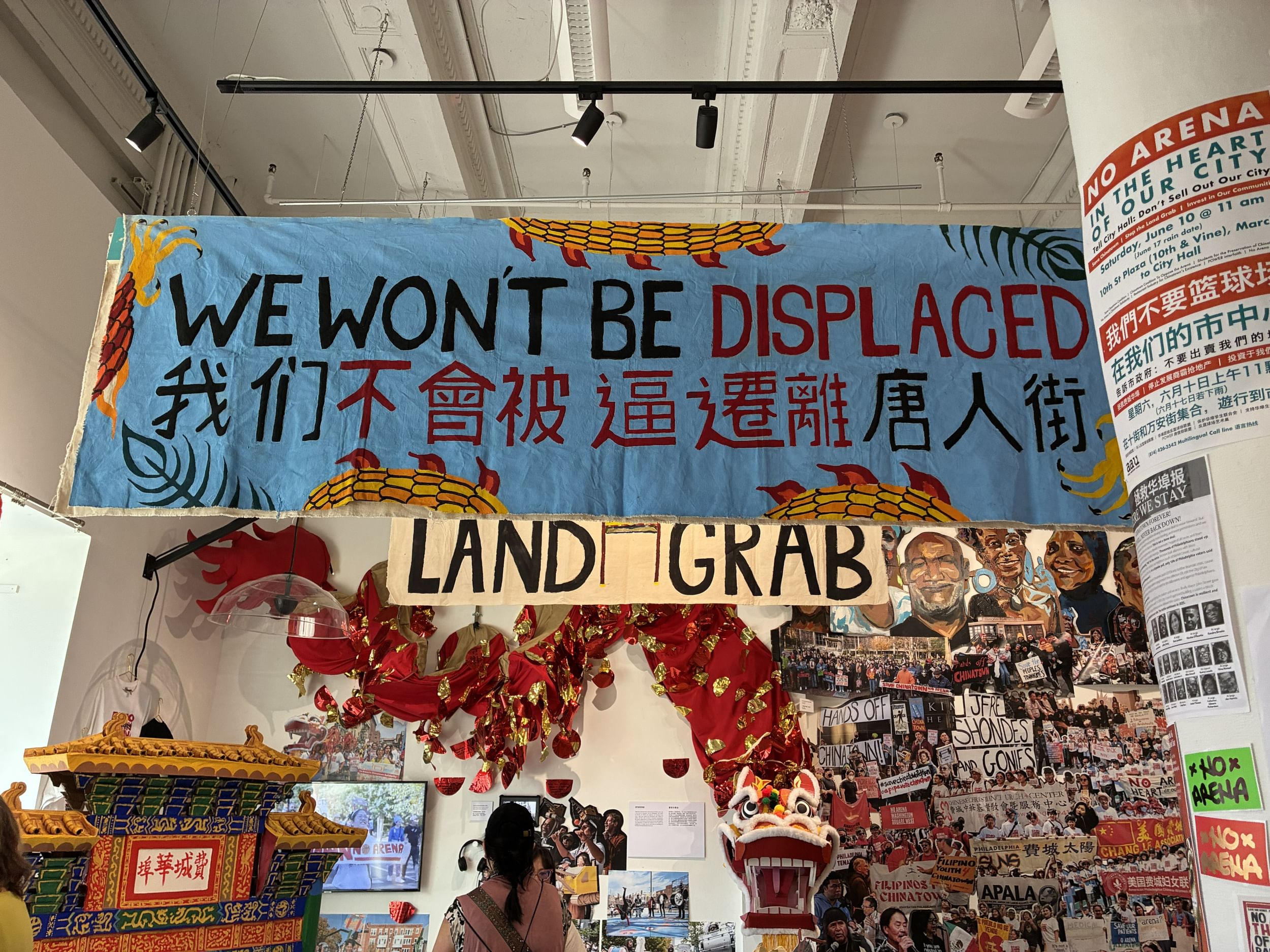 Big blue handmade banner saying We Won’t Be Displaced hangs over a gallery crammed with protest art about saving Chinatown.