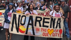 In front of a huge Chinatown protest march, 3 young Asian people hold a banner saying No arena in the heart of our city
