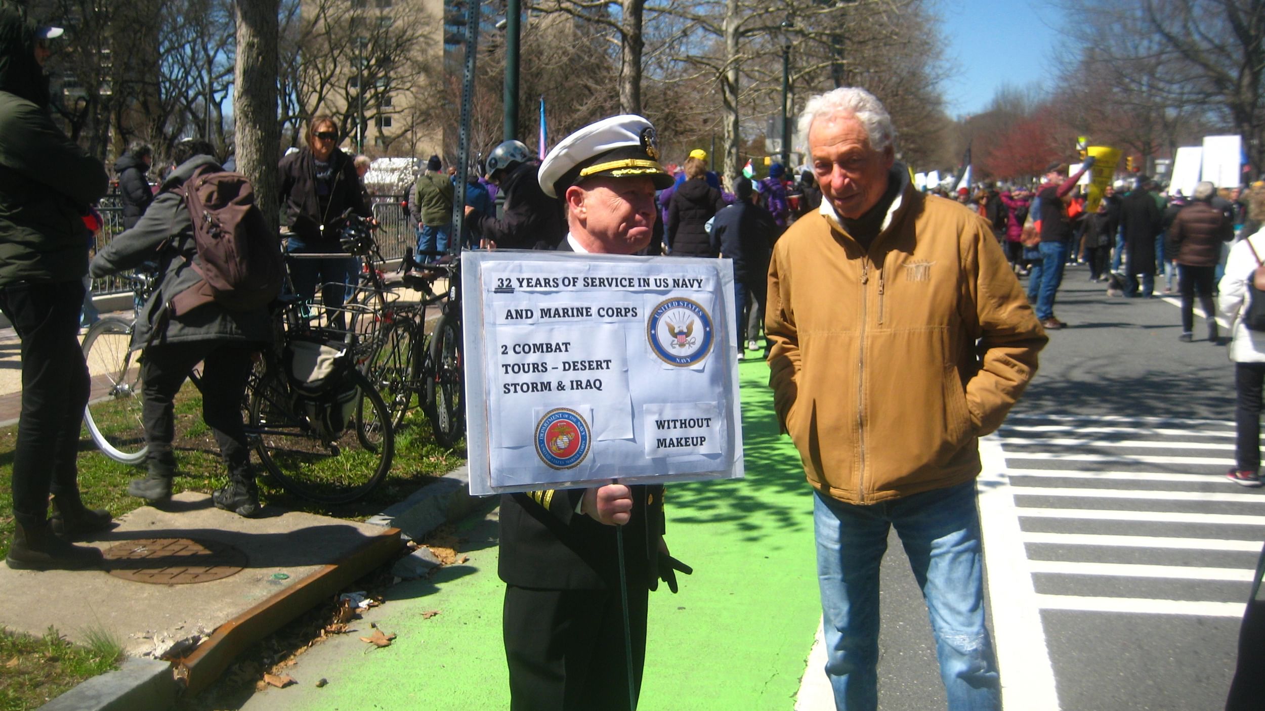 Elderly man in military dress holds a handmade sign saying he served 32 years in the Navy and Marines without wearing makeup.