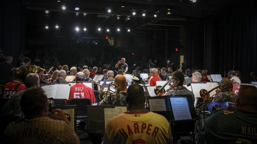 View from behind the orchestra players onstage, some wearing Philly sports jerseys, with the conductor at center.