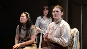 The three actors, in different costumes for their era, are grouped together onstage with concerned expressions.