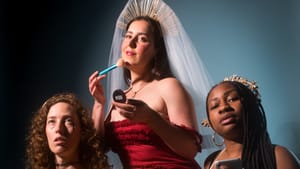 Three performers in orange, red, and white gowns respectively pose for the camera in a portrait style shot