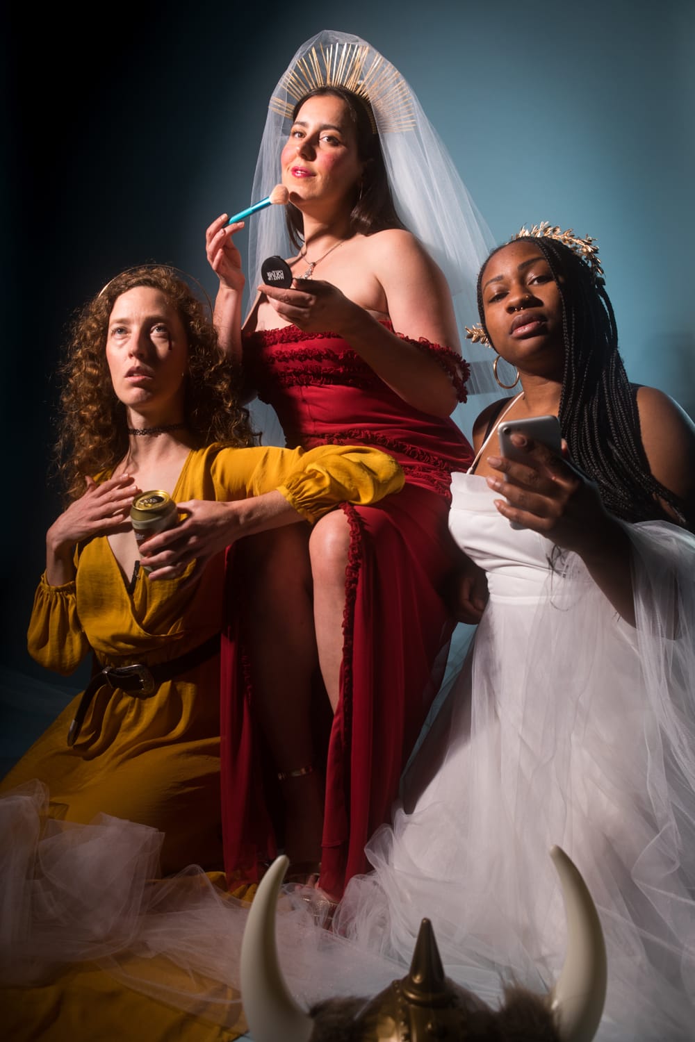 Three performers in orange, red, and white gowns respectively pose for the camera in a portrait style shot
