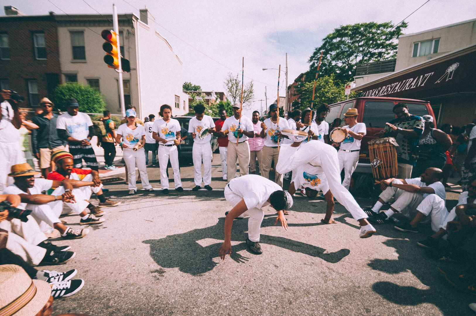 Breakdancers wearing all white in a circle of onlookers also in mostly white in a closed off street area