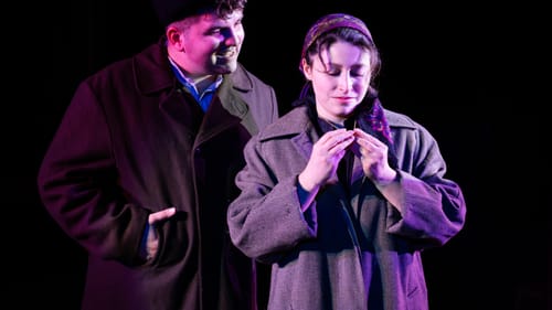 Taylor looks affectionately over Kopelove’s shoulder as she smiles into a necklace locket. They both wear long, drab coats.