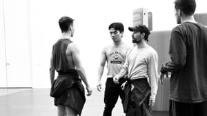 Two dancers face each other in a rehearsal room as Jesús gives instructions