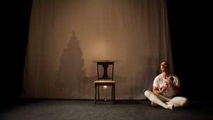 Davis, in white tee & tights, sits at right cradling a nutcracker. A chair sits at center by the shadow of a Christmas tree