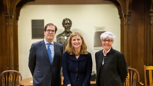 The three leaders pose smiling in a row in front of the detailed wooden interior of the event room.