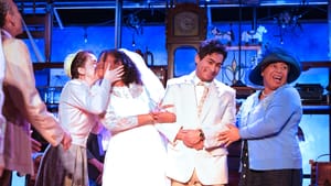 A multiracial group of five cast members create a happy, dynamic wedding-day tableau against a blue backdrop.