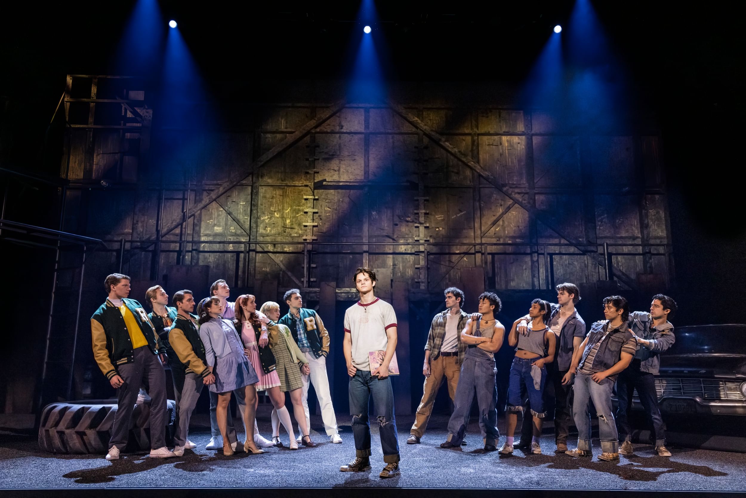 White stands at center in dirty white tee and jeans; the ensemble leans away from him in a V, preppy (left) & grungy (right)