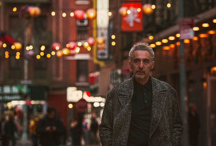 Turturro, a 69-year-old white man in a tweedy gray jacket, walks through New York’s Chinatown.
