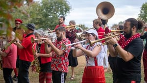 A band dressed in mostly blacks and reds play various wind instruments outside in a park