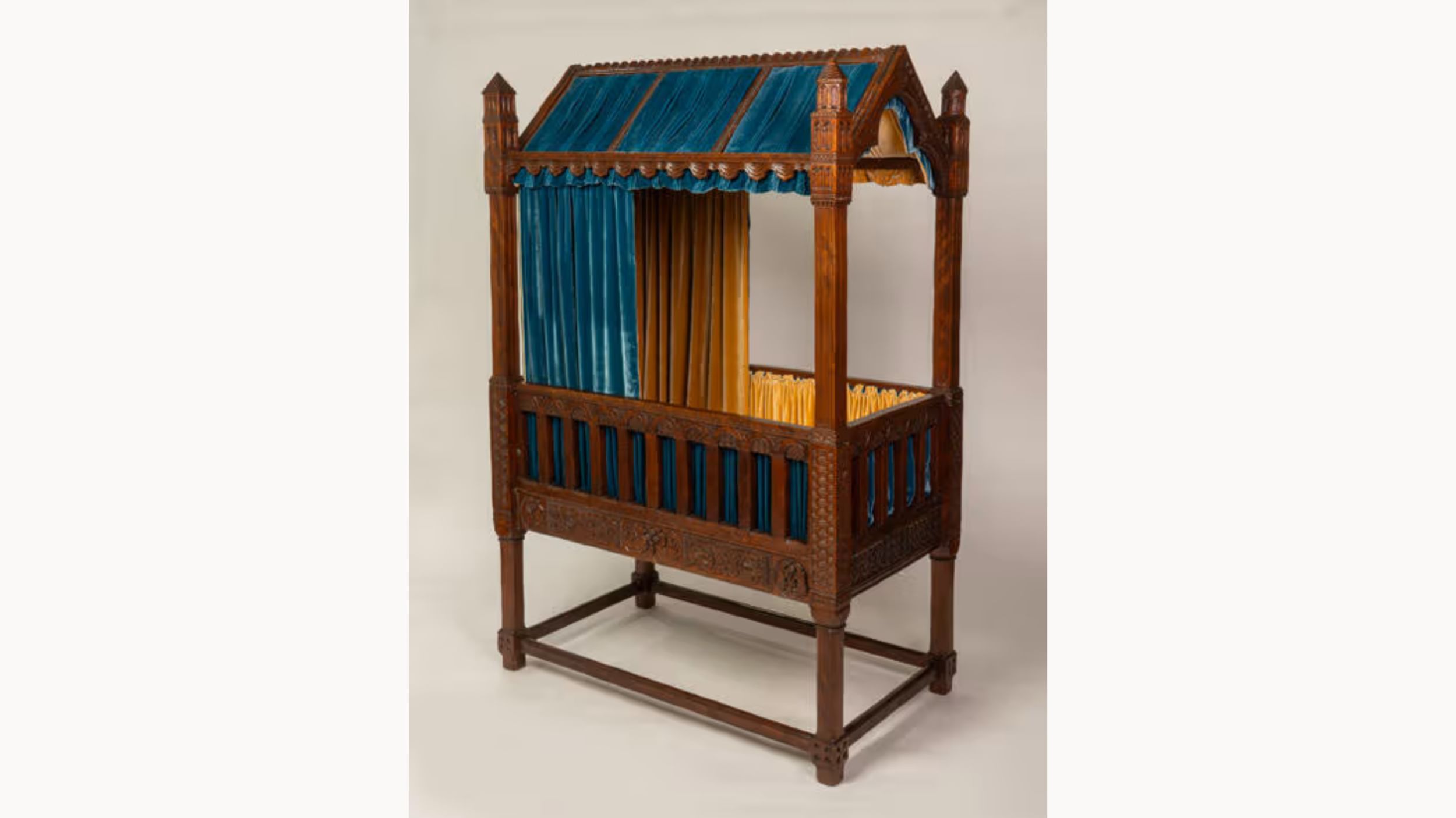 Royal-looking dark wooden crib in four-poster bed style, with turquoise and yellow velvet curtains.