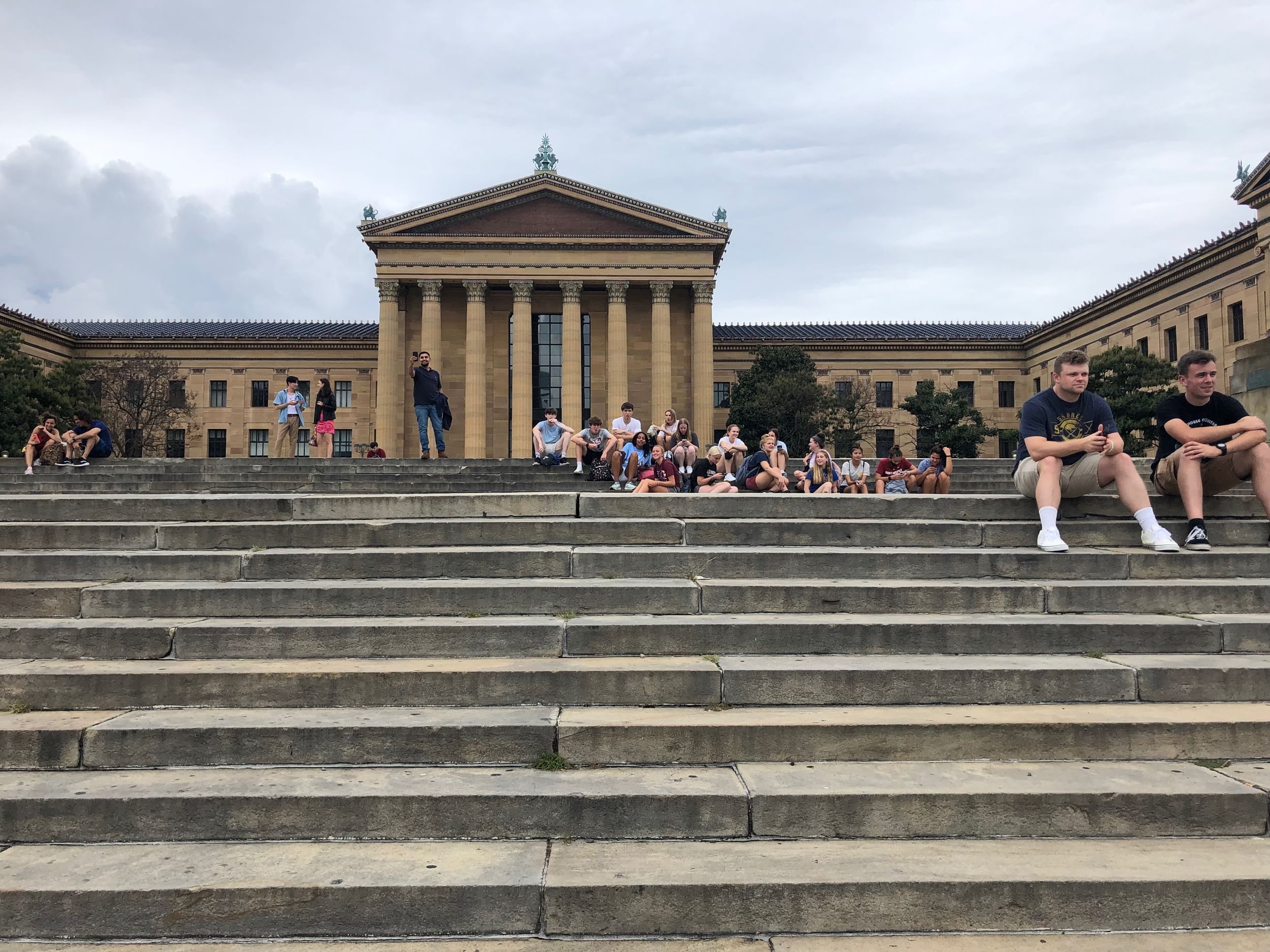 View from partway down the museum’s famous steps, looking up at the brown columned façade, with groups of people sitting.
