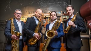 The PRISM Quartet. Four white men in suits each hold a gold-colored saxophone of a different type and size.