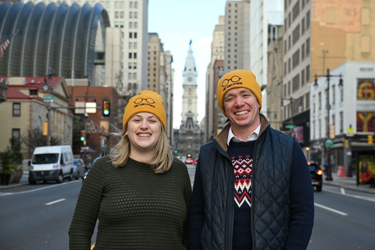 Moskowitz and Dobrowsky pose smiling on Broad Street, City Hall behind them, wearing yellow Ijames beanies.