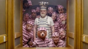 A group of 13 older men in matching striped pajamas stand behind Paddington, the CG-animated bear, looking to the camera