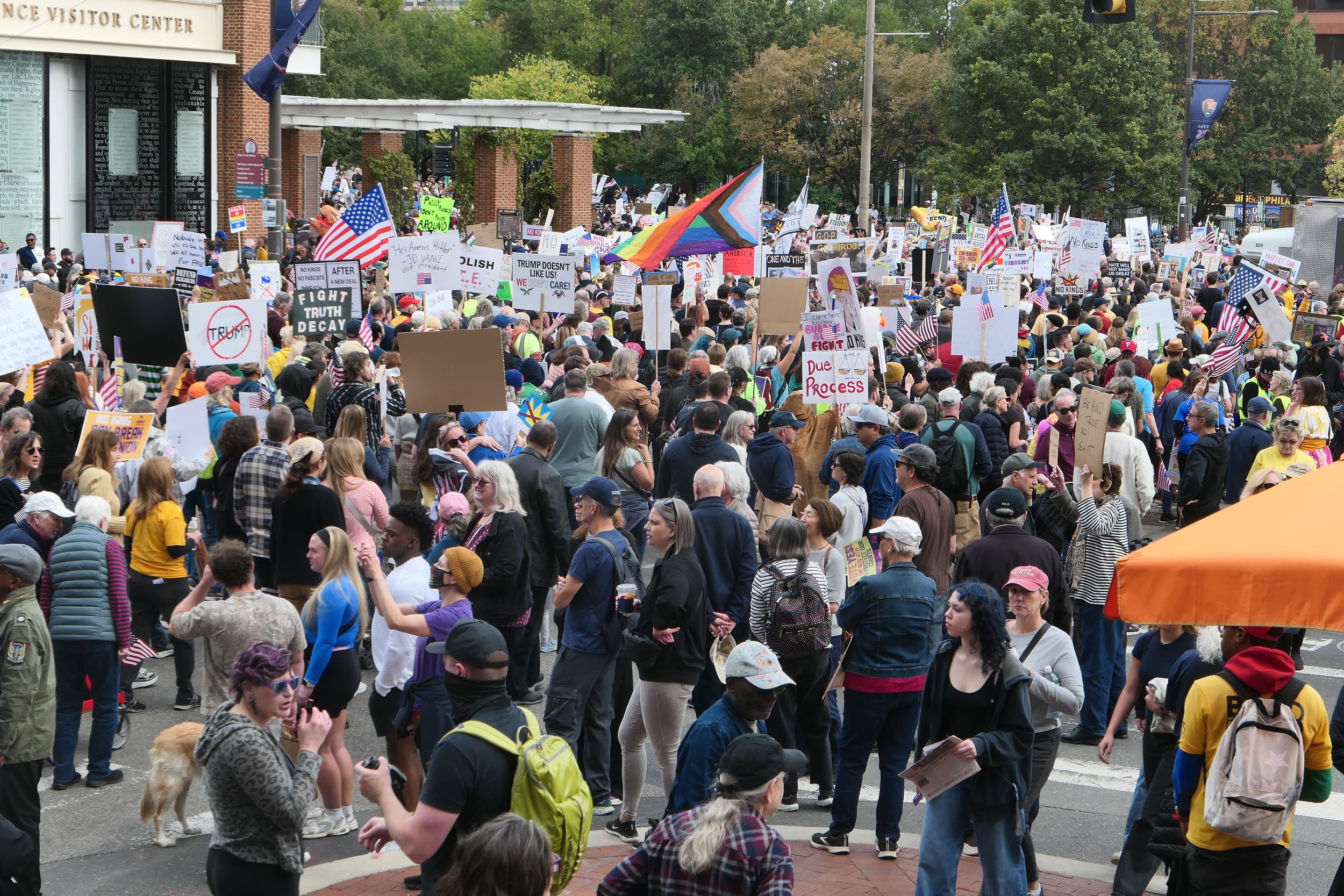 A huge crowd gathers outside the brick Independence Visitor Center, with a giant Philly Pride flag and American flags visible