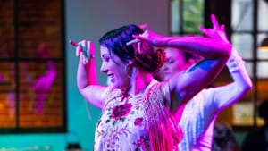 Two dancers in mid-step in an indoor space, with warm, purple-tinted lighting