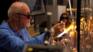 Stankard wears dark protective eyewear, using fire from a torch to shape glass in a laboratory setting