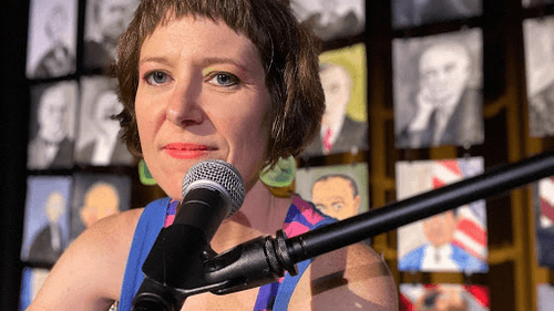 Bondurant, a white woman with short brown hair, poses next to a mic with childlike illustrations of Presidents behind her.