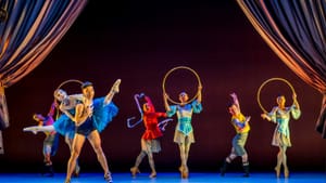 Seven dancers in colorful, iridescent circus-evoking costumes, women en pointe, wield hoops and ribbons.