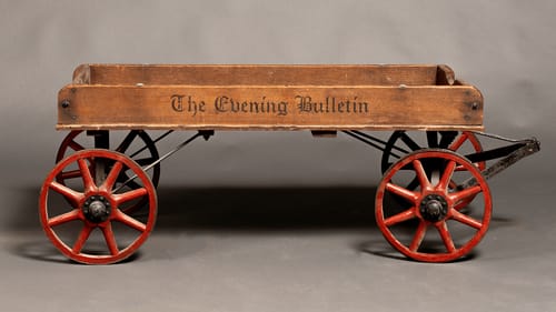 Side view of the vintage wooden wagon with low sides and large red spoked wheels.