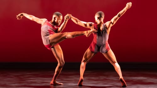 Two Black male dancers in patterned red & gray leotards clasp hands and strike different dramatic poses with limbs outspread