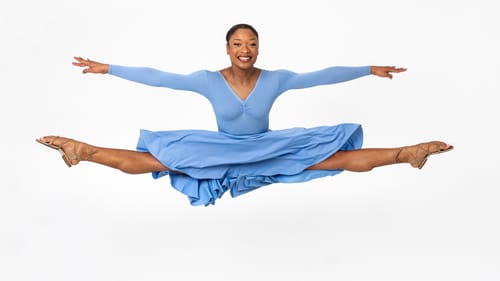 Davis, a Black dancer in strappy brown sandals & blue dress, leaps into a split while her skirt flies weightlessly around her