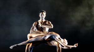 Gilbert squats with Fenton lying gracefully extended across his knees. They both wear bronze, silver & gold bodysuits.