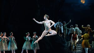 With right leg & arm outstretched & the others angled, a smiling Roxander seems to hover in the air in front of the ensemble