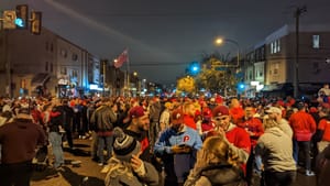 A nighttime photo of Broad Street packed with hundreds of baseball fans, many wearing red. A flag flies above the crowd.