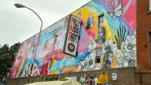 Philly AIDS Thrift sign outside on side of building wall that has a large mural painting with floral art, colors, portraits